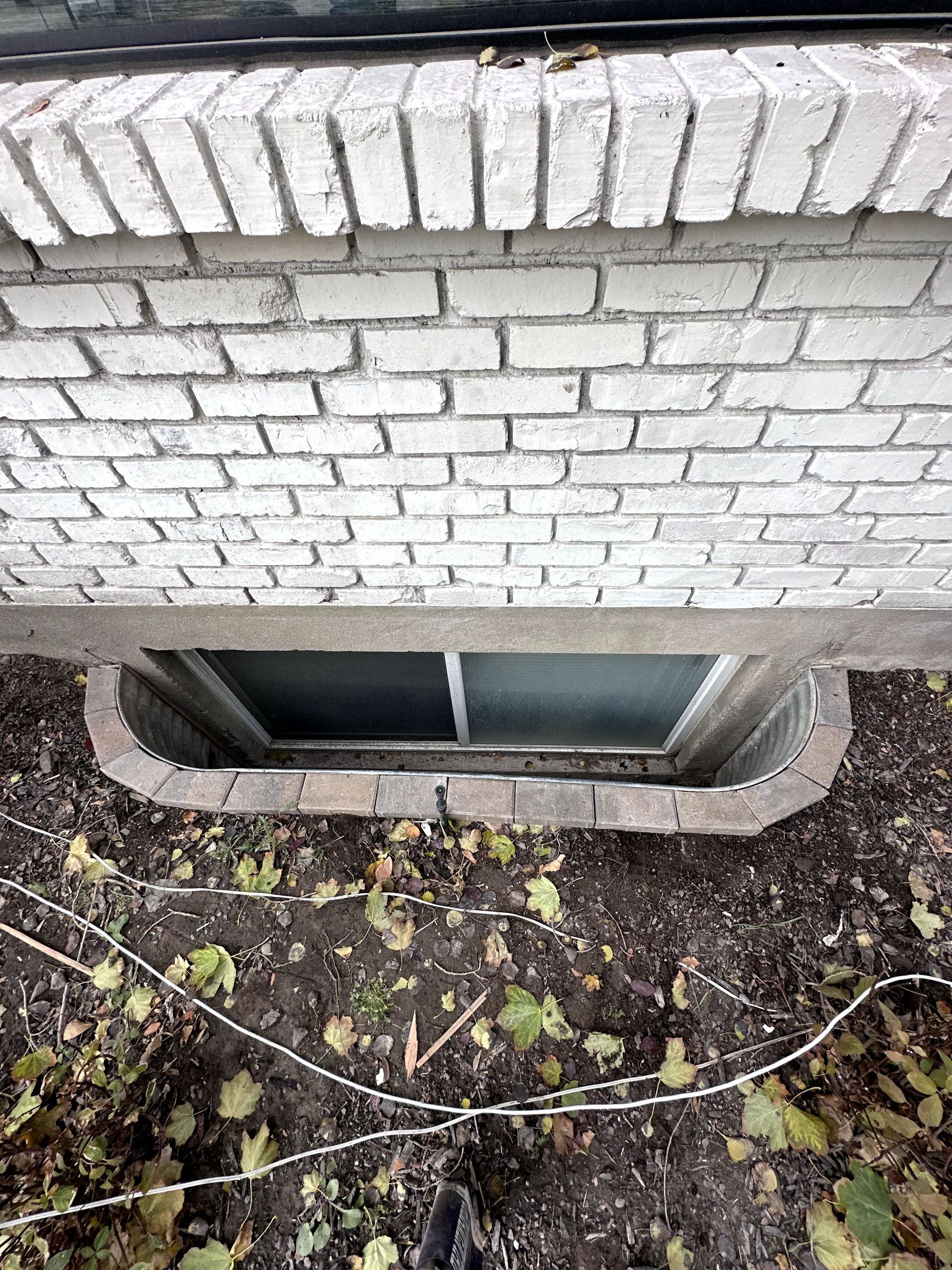 A white brick building with a window in the basement.