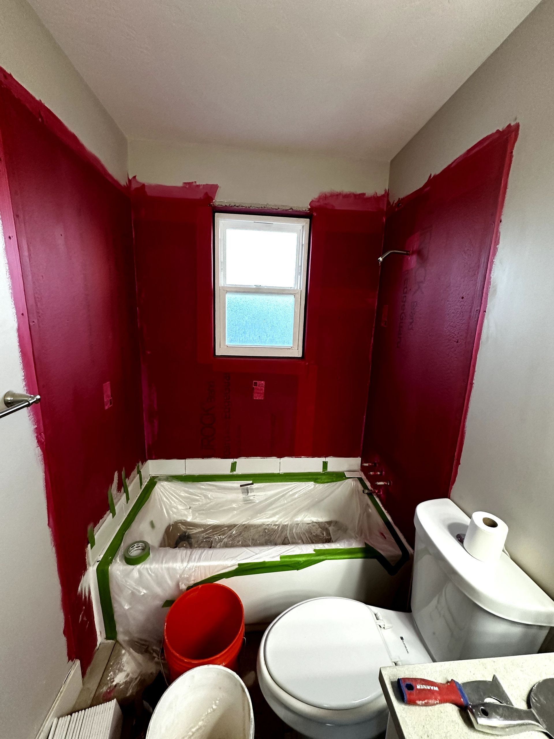 A bathroom with red walls , a toilet , and a bathtub being painted.
