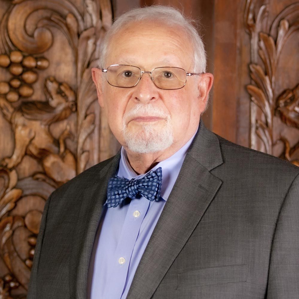 A man in a suit and bow tie is standing in front of a carved wall.