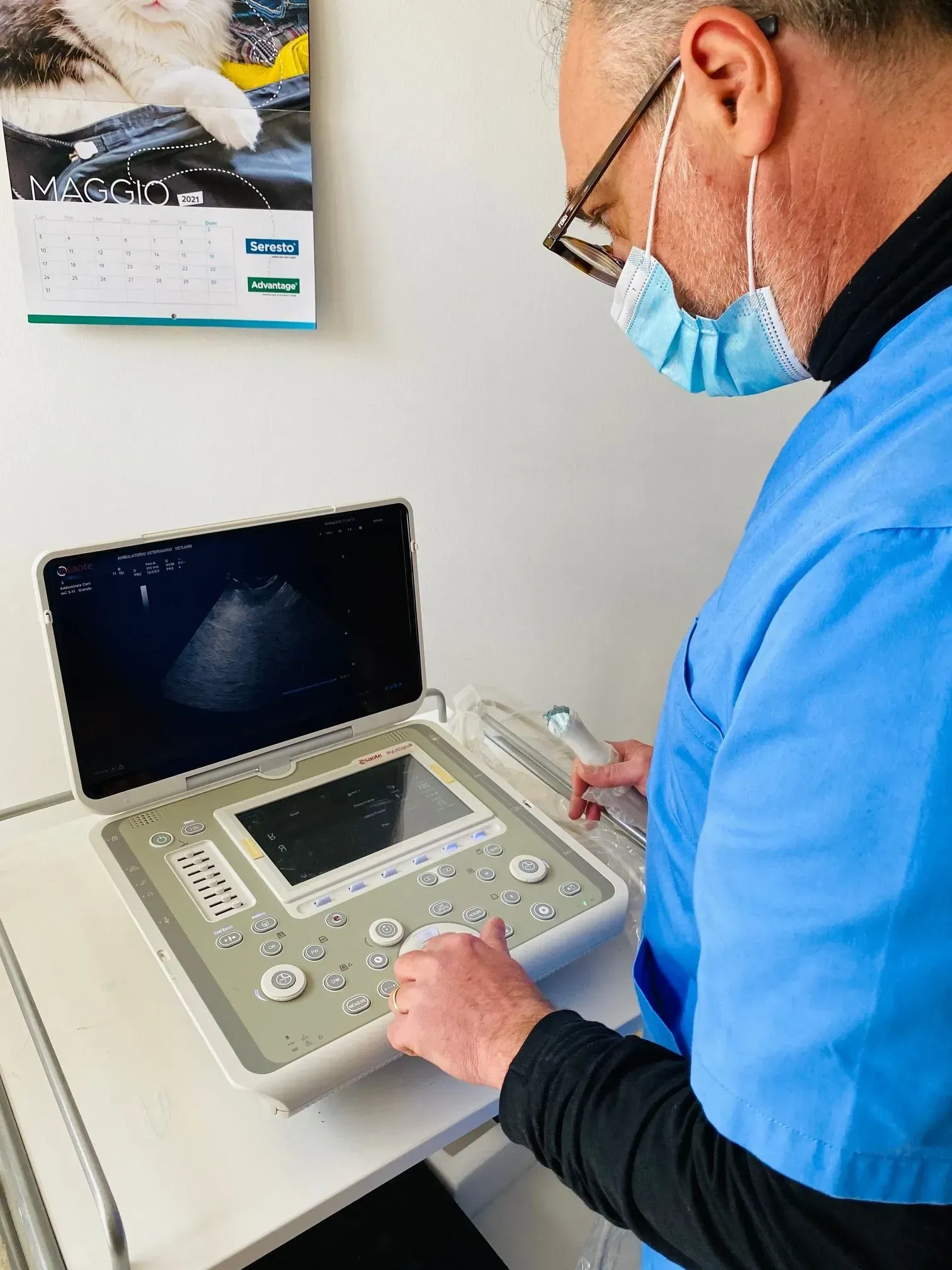 Un operatore sanitario in camice blu e mascherina utilizza un ecografo portatile.