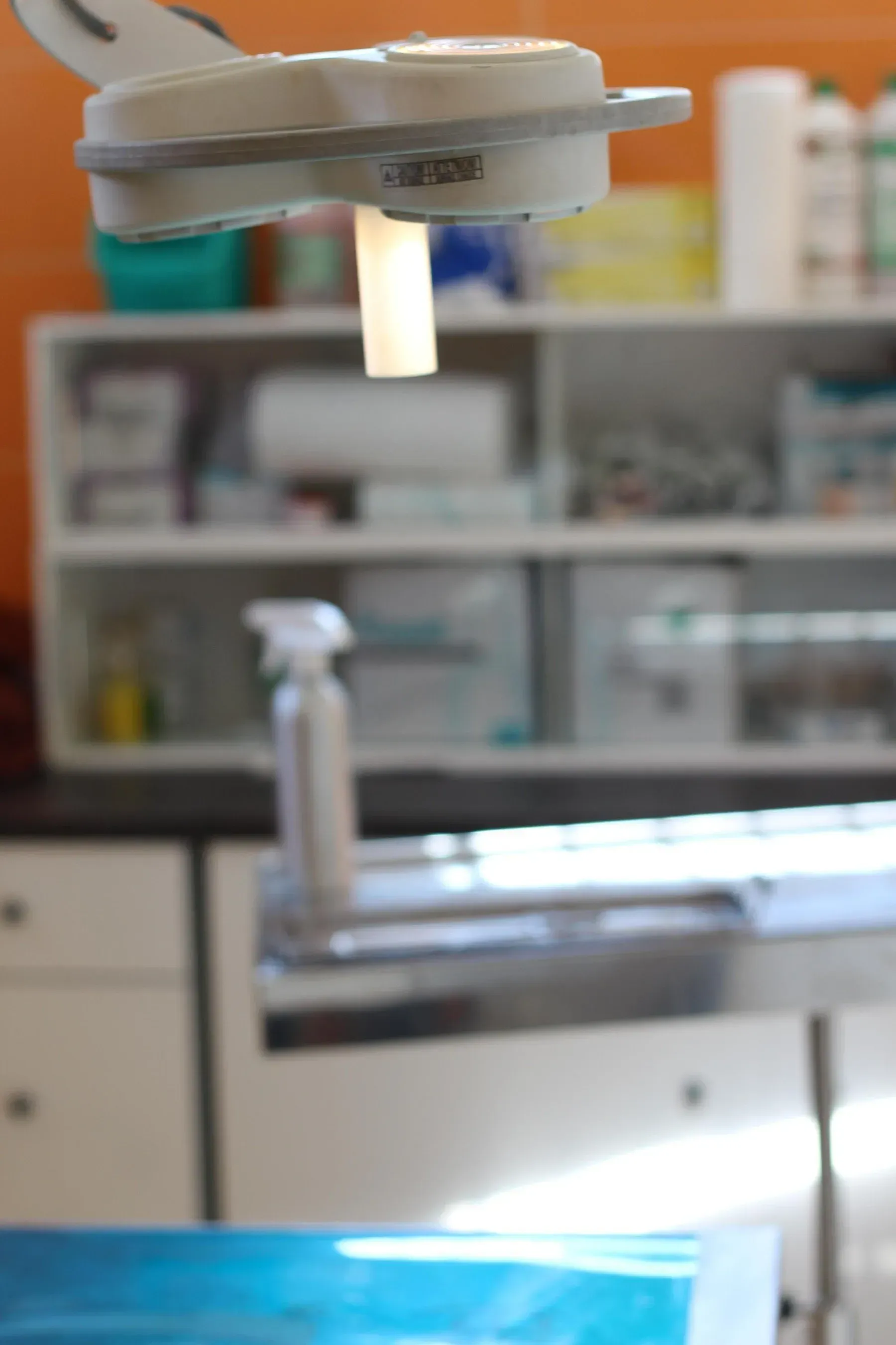 Una lampada clinica luminosa illumina un lettino da visita sterile, sullo sfondo del quale si trovano degli scaffali con forniture mediche.