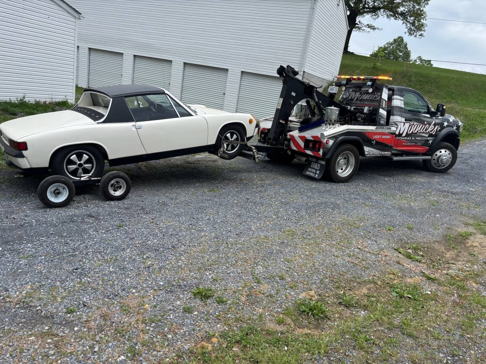 White sports car being towed by a tow truck on a gravel driveway.