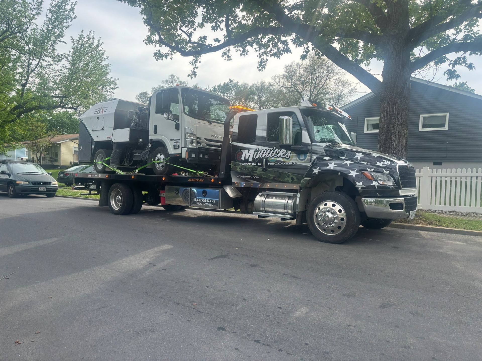 Tow truck with a small truck loaded on the flatbed, parked on a residential street.