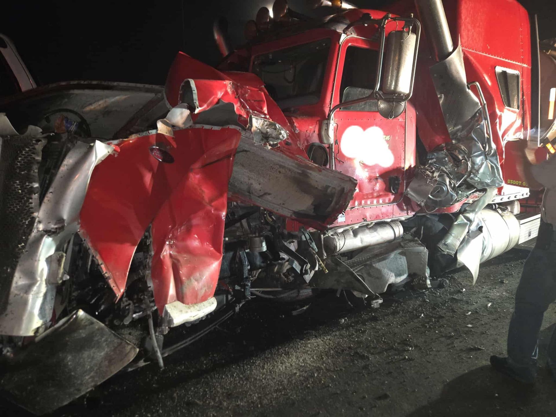 Damaged red semi-truck involved in a collision at night; vehicle severely crumpled.