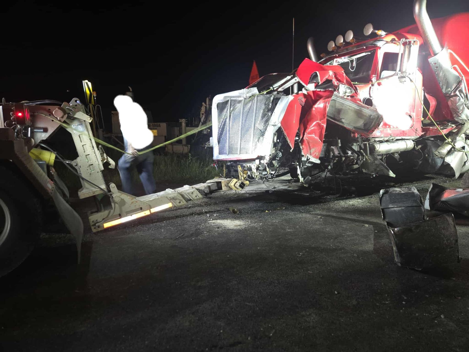 Severely damaged red semi-truck at night, being towed away.