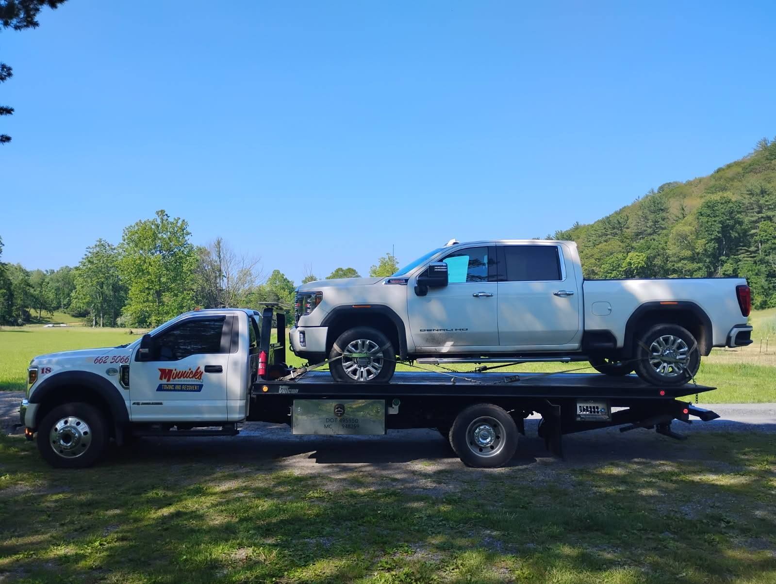 White tow truck carrying a white pickup truck on a sunny day.