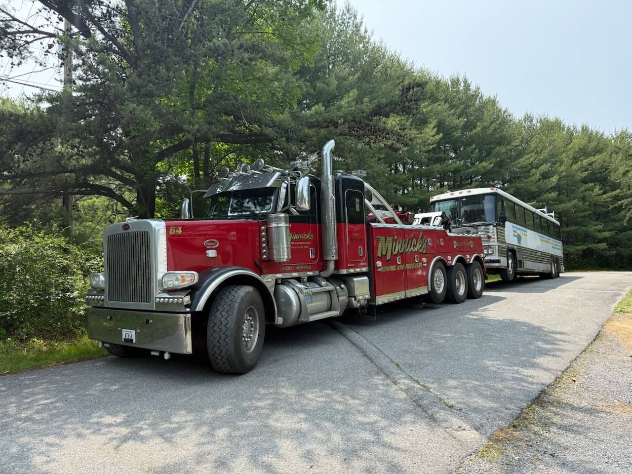 Red tow truck towing a bus on a paved road, trees in the background.