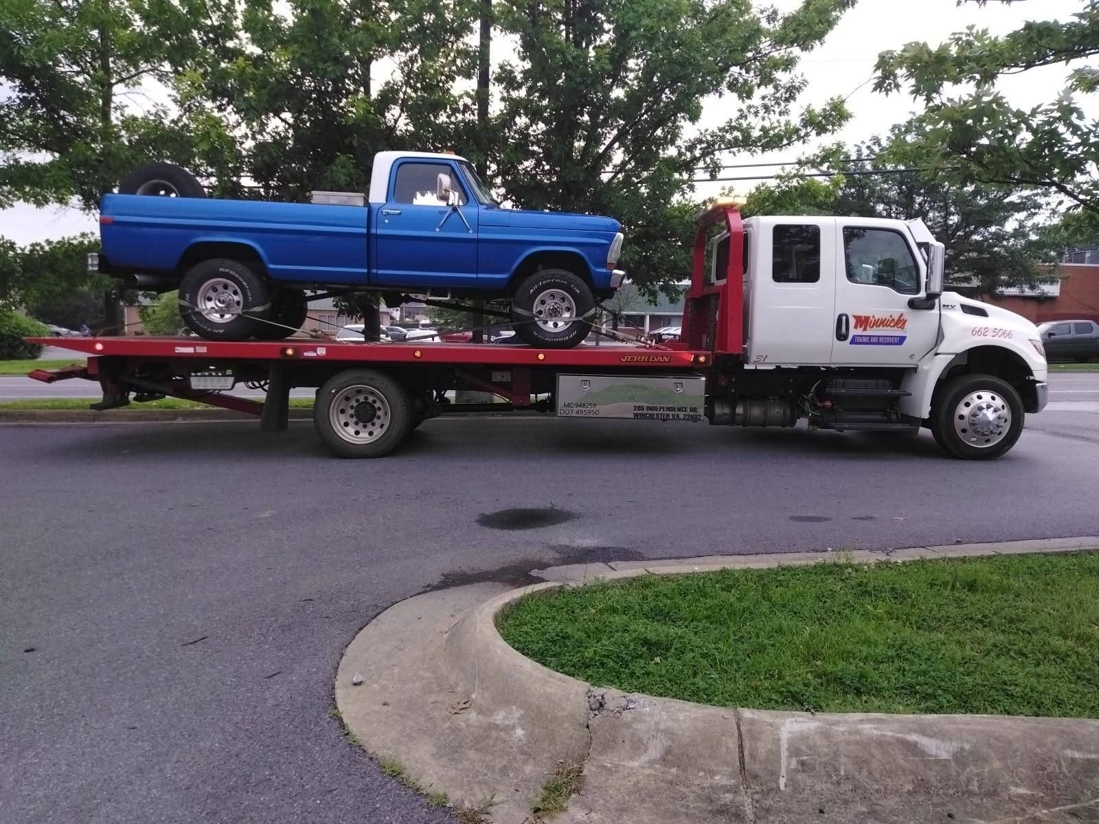 A blue vintage Ford truck being transported on a red flatbed tow truck.