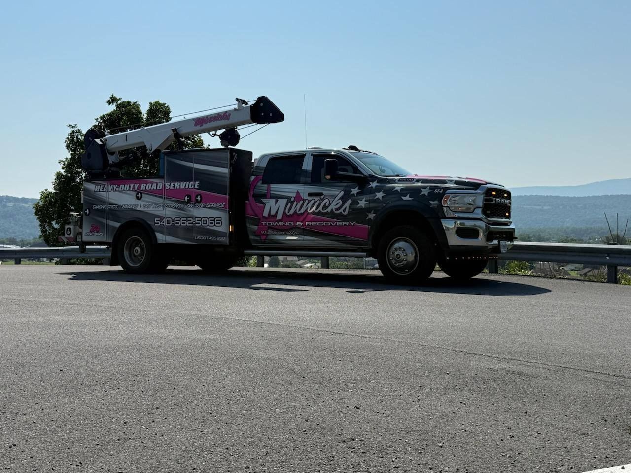 Utility truck with crane and company logo on asphalt road overlooking a distant landscape.