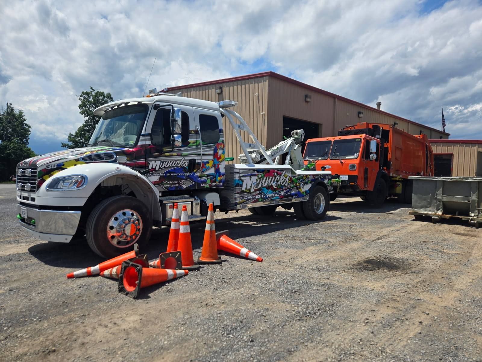 Tow truck pulling an orange trash truck; cones on ground. Building in the background.