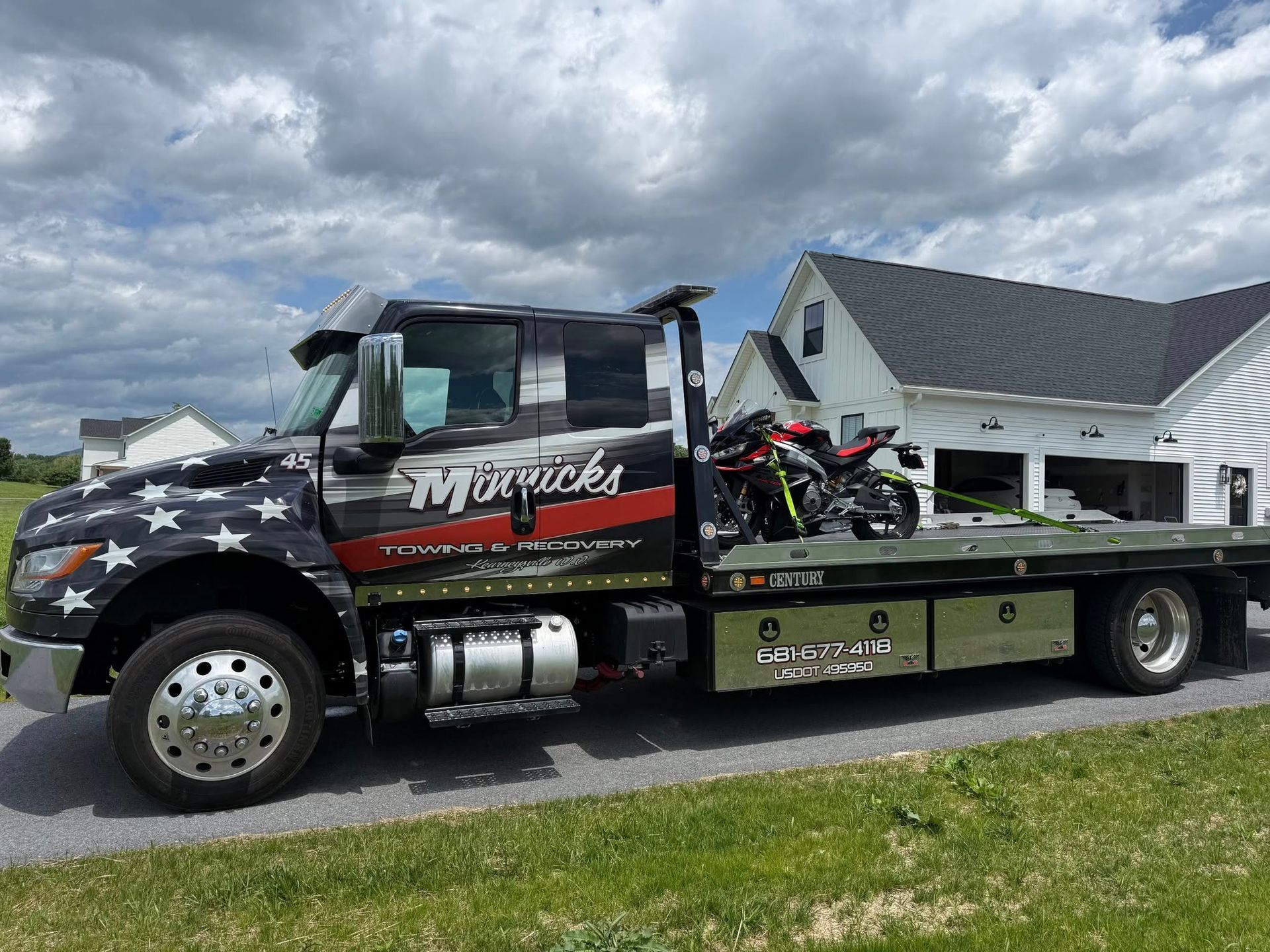 Tow truck with a red and black motorcycle on its flatbed, parked in front of a white house.