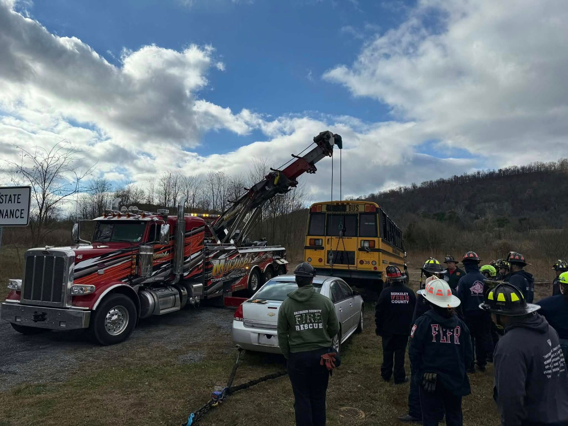 Tow truck at a crash site, lifting a school bus. Firefighters assess damage near a silver car.