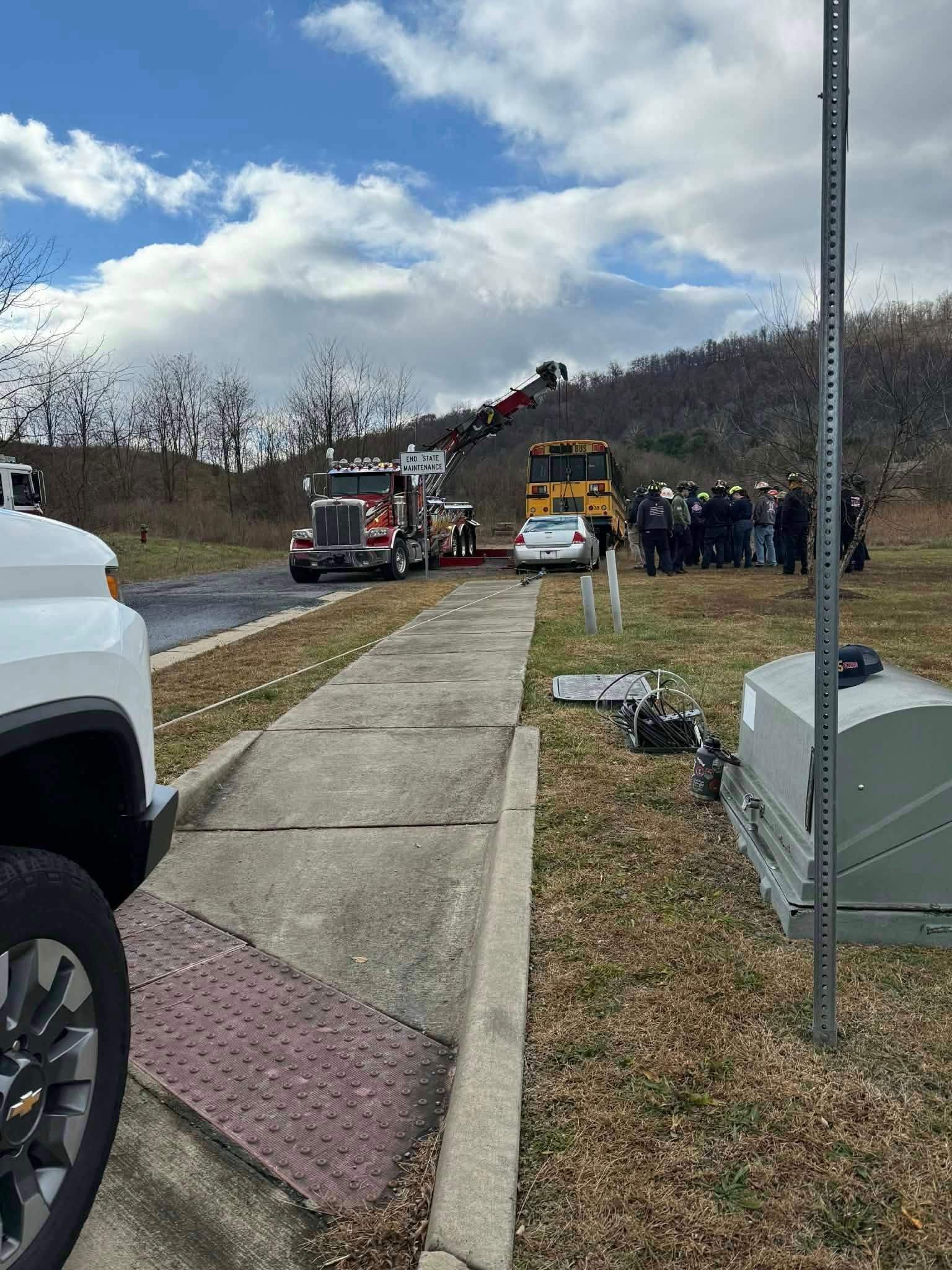 Trucks and emergency vehicles at a scene with a hill in the background. Several people are present.