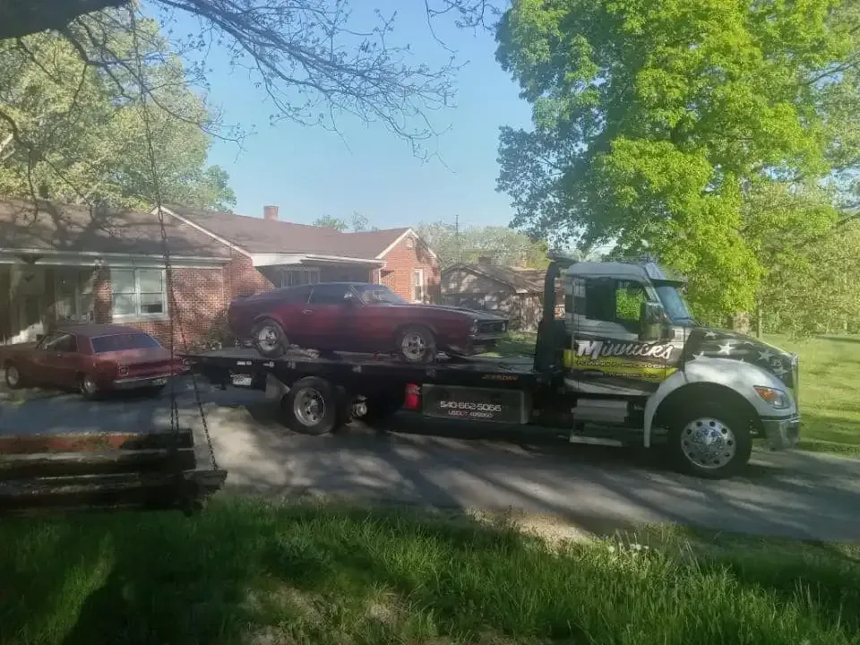 Tow truck carrying two red classic cars parked in front of a house.