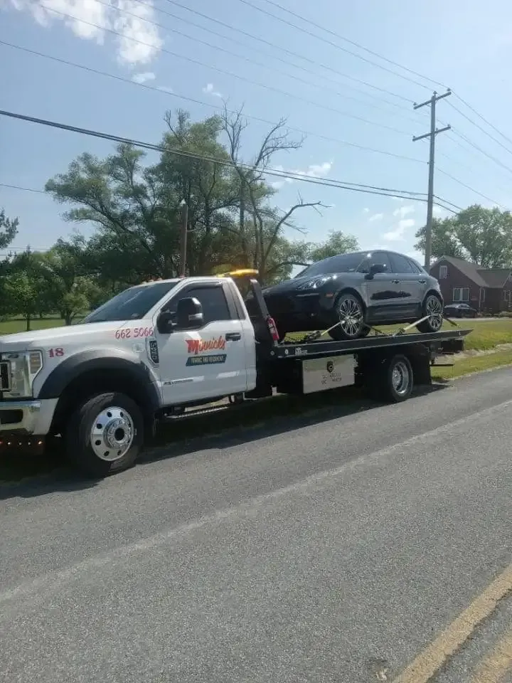 Tow truck transporting a silver car on a sunny day.