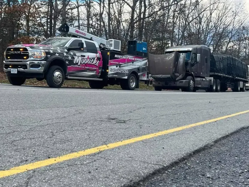 Tow truck towing a semi-truck with damaged hood on a road with a yellow line.