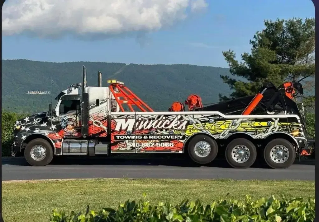 Tow truck with custom graphics and orange boom, parked on a road with a mountain backdrop.