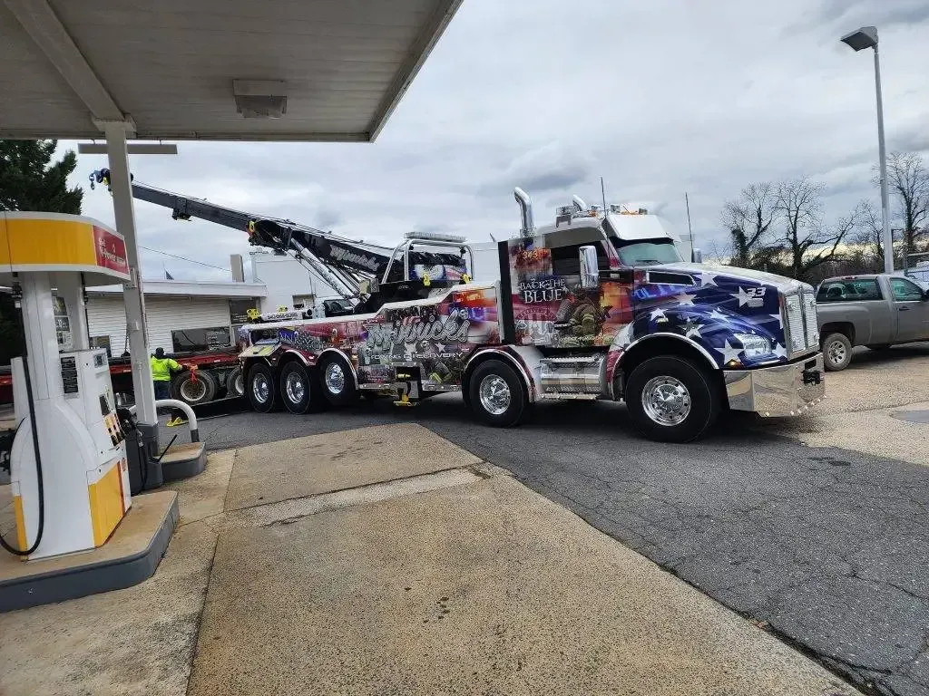 Large, colorful tow truck at a gas station, with a boom extended.