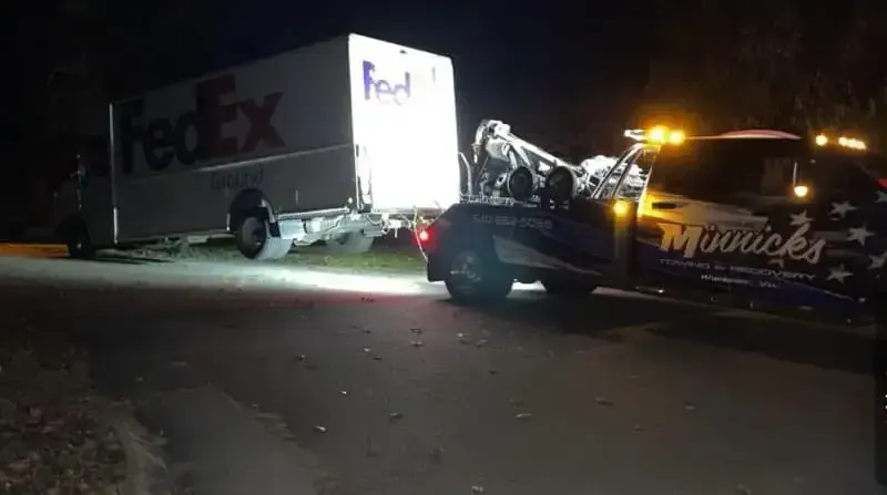 A FedEx truck being towed at night by a tow truck.