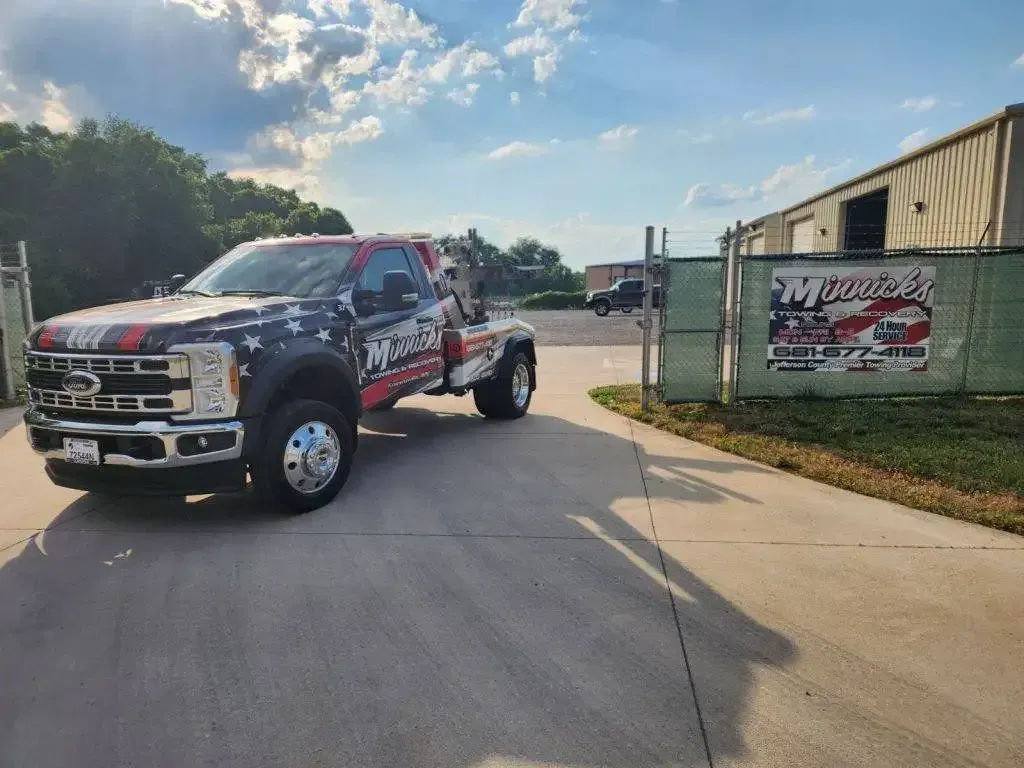 Tow truck with American flag design parked near a building with a sign.