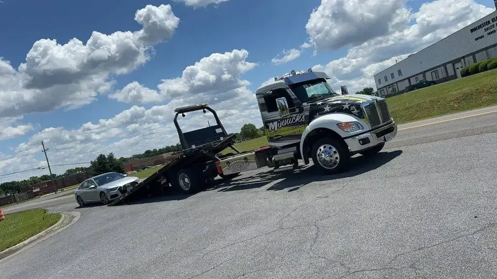 Tow truck loading a silver car on a sunny day.