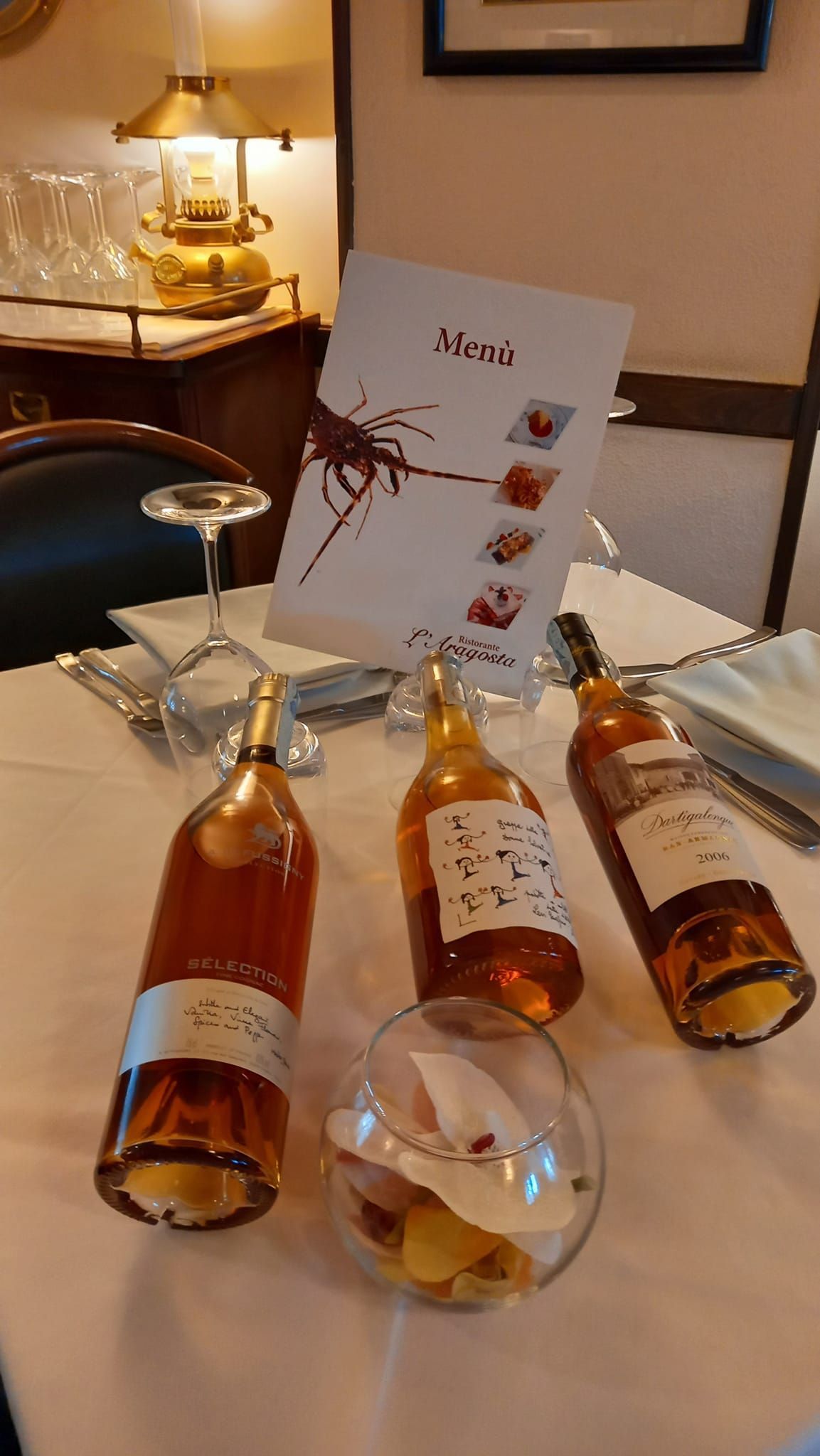 Apparecchiatura del tavolo in un ristorante con tre bottiglie di vino, menù, bicchieri e una ciotola di caramelle.