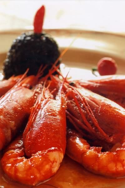 Gamberi rossi su un piatto con guarnizione scura e una bacca rossa.