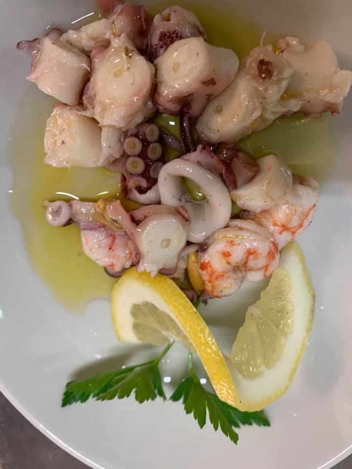 Insalata di polpo con spicchi di limone e prezzemolo su un piatto bianco, condita con olio d'oliva.