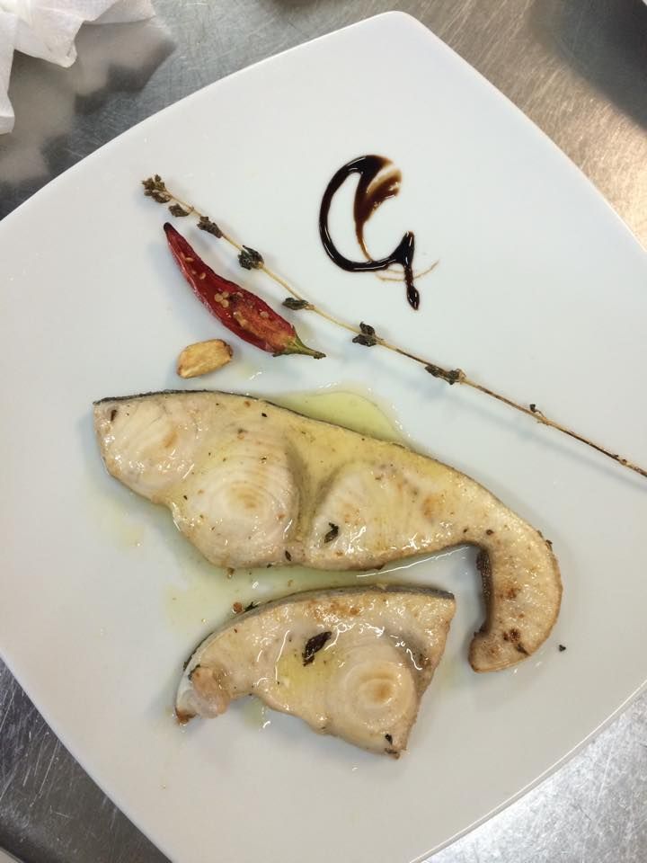 Trancio di pesce spada alla griglia con contorno su un piatto bianco.