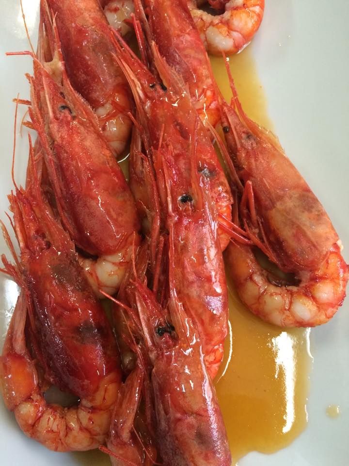 Gamberi rossi cotti su un piatto bianco, luccicanti di salsa.