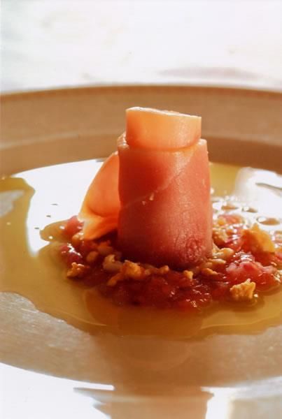 Una torre di prosciutto arrotolato su un letto di pomodoro e briciole, con una salsa dorata circostante, su un piatto beige.