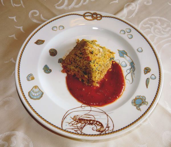 Pezzo di cibo quadrato con salsa rossa su un piatto con motivo nautico.