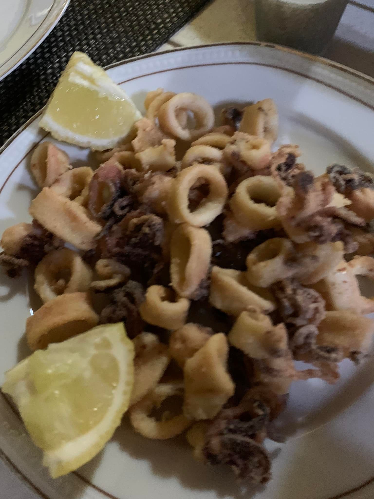 Calamari fritti con spicchi di limone su un piatto bianco.