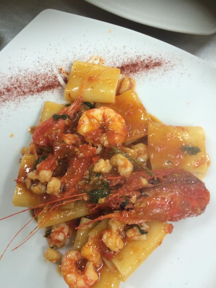Pasta con gamberi in salsa di pomodoro su un piatto bianco, cosparsa di polvere rossa.