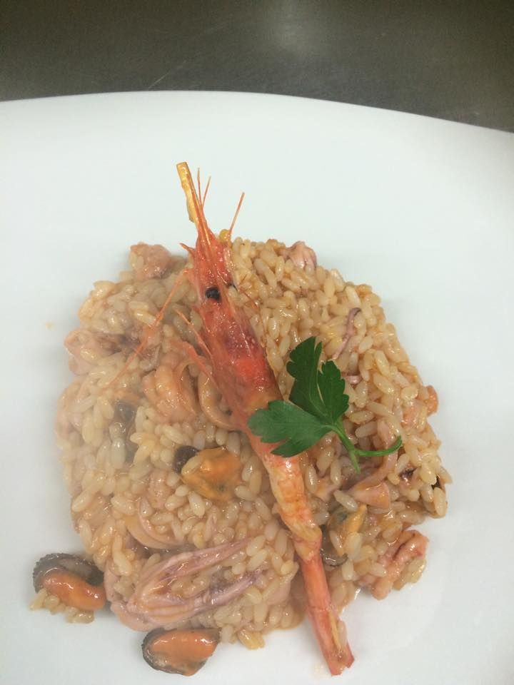 Risotto ai frutti di mare con contorno di gamberi su un piatto bianco.