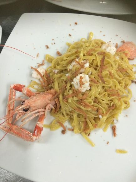 Piatto di pasta con uno scampo grande e briciole marroni sparse su un piatto bianco.