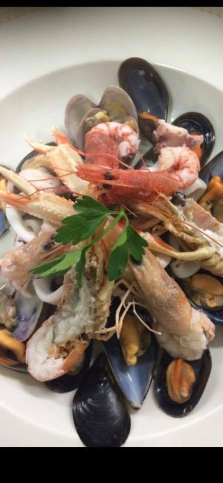 Piatto di frutti di mare servito su un piatto bianco. Include cozze, gamberi e altri molluschi.