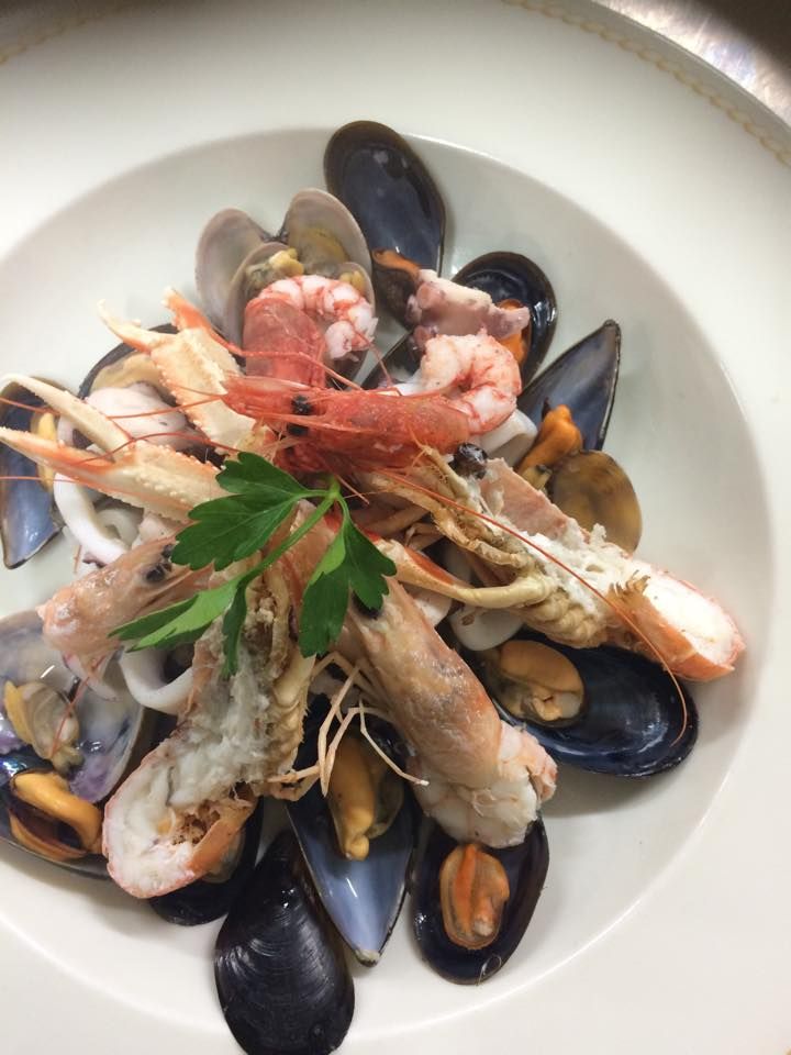 Piatto di frutti di mare con cozze, vongole, gamberi e prezzemolo come guarnizione in una ciotola bianca.
