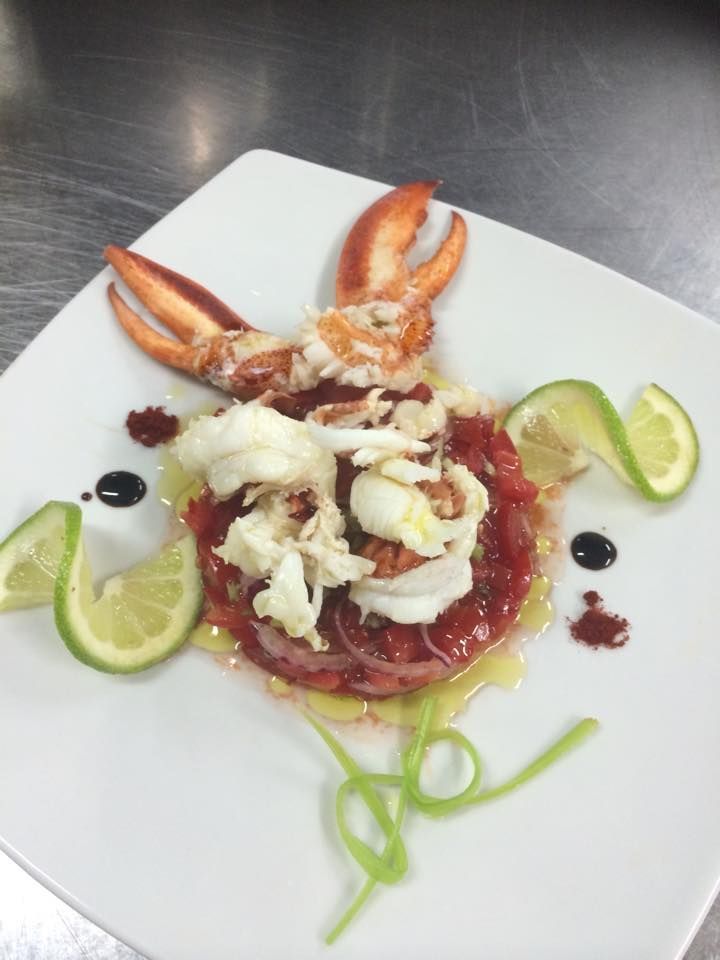 Chela e carne di aragosta su un piatto rosso su un piatto bianco con spicchi di lime e guarnizioni.