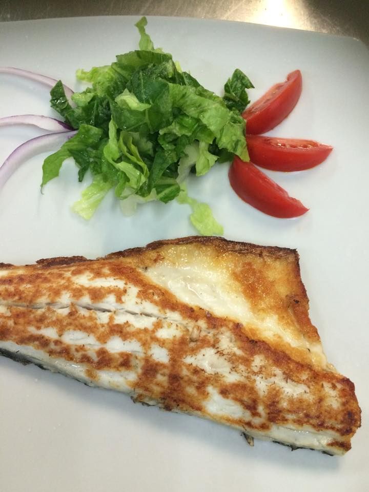 Filetto di pesce scottato in padella con contorno di insalata di lattuga, pomodori e cipolla rossa su un piatto bianco.