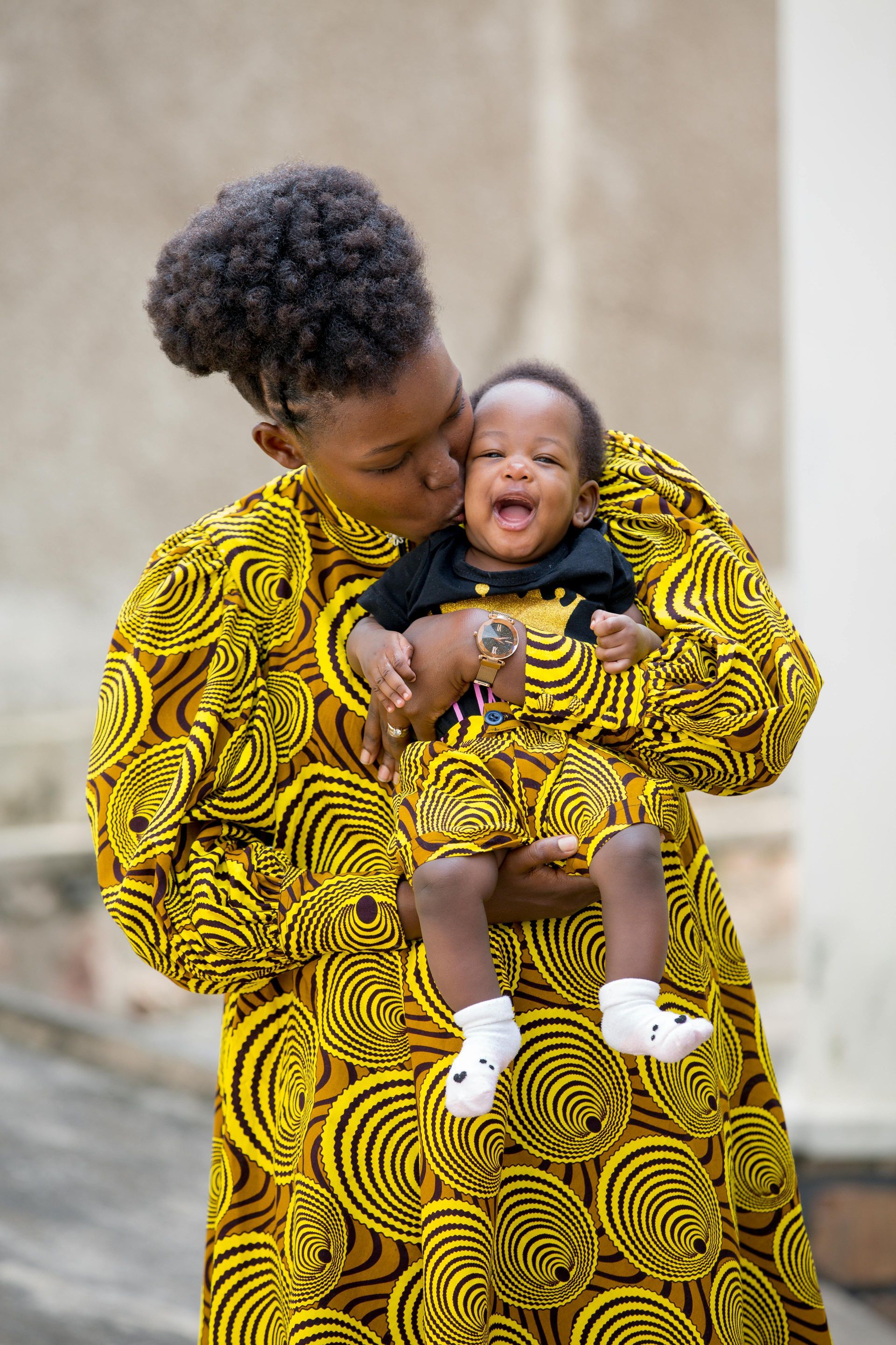A woman in a yellow dress is holding a baby in her arms.