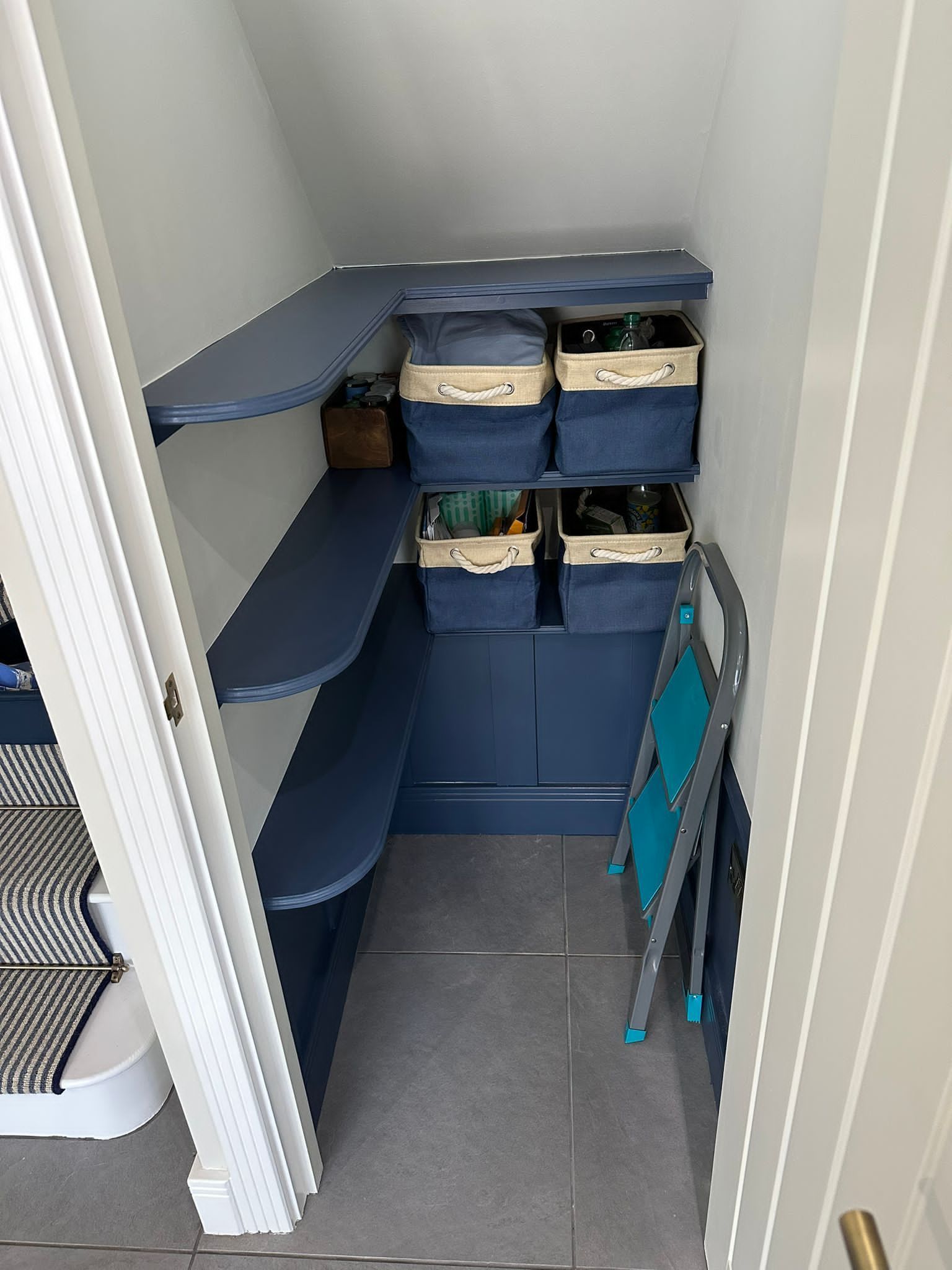 a small closet under a staircase with shelves and baskets .