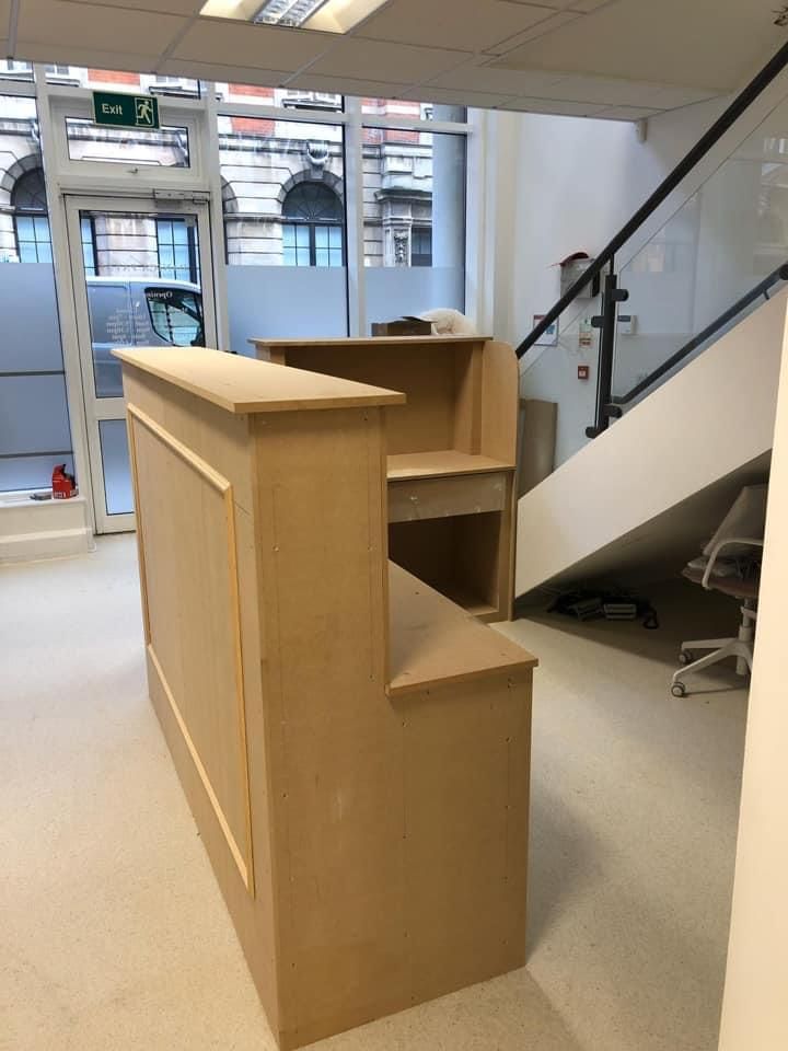a wooden desk in a room with stairs and a green exit sign