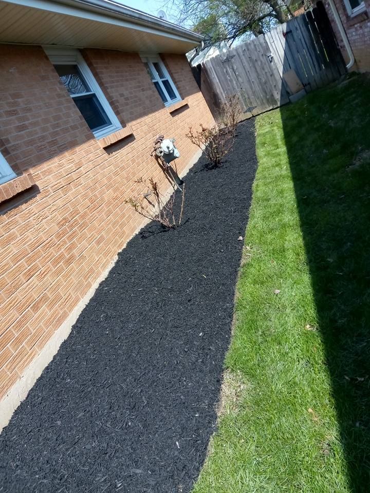 A narrow landscape bed with fresh black mulch running along the brick wall of a house, next to a green grass lawn.