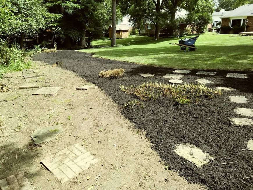 A backyard project showing a transition from bare dirt to a new mulch garden bed with stone pavers laid out in a path.