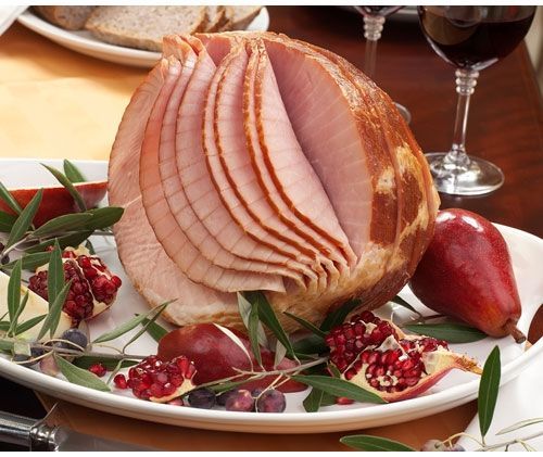 A white plate topped with sliced ham pears and pomegranates