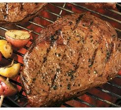 A steak is cooking on a grill with potatoes.