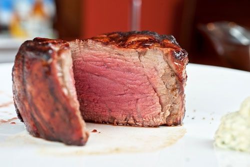 A steak with a slice taken out of it is on a white plate.
