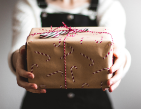 A woman is holding a gift wrapped in brown paper with candy canes on it.