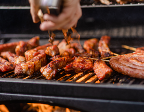 A person is cooking meat on a grill with tongs.